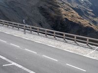 there is a bike rider on a winding street near a mountain range, and a car