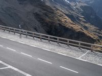 there is a bike rider on a winding street near a mountain range, and a car