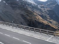 there is a bike rider on a winding street near a mountain range, and a car