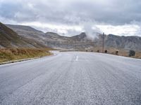 a large long empty road that leads to the top of a mountain with mountains and a sky in the background