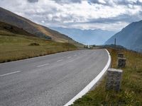 the view of a country side road with mountains in the background and cloudy sky above