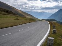 the view of a country side road with mountains in the background and cloudy sky above