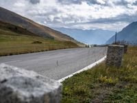 the view of a country side road with mountains in the background and cloudy sky above