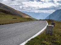 the view of a country side road with mountains in the background and cloudy sky above