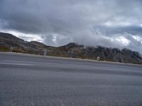 a motorcycle parked on the side of a road on a cloudy day near mountains and clouds