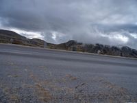 a motorcycle parked on the side of a road on a cloudy day near mountains and clouds