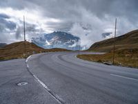 an asphalt road stretches into the distance with mountains in the background on a cloudy day