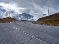 an asphalt road stretches into the distance with mountains in the background on a cloudy day