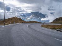 an asphalt road stretches into the distance with mountains in the background on a cloudy day