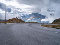 an asphalt road stretches into the distance with mountains in the background on a cloudy day