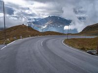 an asphalt road stretches into the distance with mountains in the background on a cloudy day