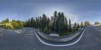 the wide shot of a curved road in the mountain above trees as seen from the inside of the circular image