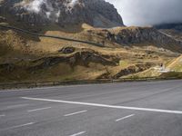 a view of mountains from an empty highway, in the middle of the frame, while it looks overcast