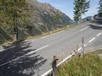 a black motorcycle driving on an empty street next to mountains and trees in a field