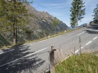 a black motorcycle driving on an empty street next to mountains and trees in a field