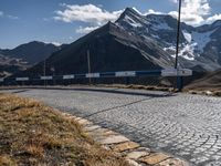 a person standing on the side of a mountain road next to a paved road with a bunch of poles and a sky