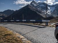 a person standing on the side of a mountain road next to a paved road with a bunch of poles and a sky