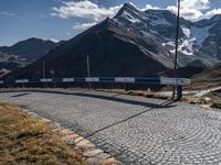 a person standing on the side of a mountain road next to a paved road with a bunch of poles and a sky