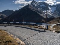 a person standing on the side of a mountain road next to a paved road with a bunch of poles and a sky