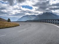 a wide road in the mountains with some clouds in the sky and mountains behind it