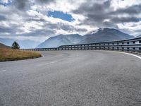 a wide road in the mountains with some clouds in the sky and mountains behind it