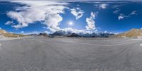 a 360 - shot of an asphalt road with a sky background and snow capped mountains in the distance