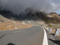 a highway in a high mountain area with some clouds above it and a man on the side