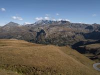 the grass is dying to the side of the mountains, with a mountain top in the distance