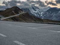 a road that is on the side of a mountain with snow capped mountains around it