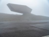 a car driving on the road during the foggy day in front of a large object