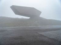 a car driving on the road during the foggy day in front of a large object