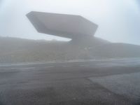 a car driving on the road during the foggy day in front of a large object