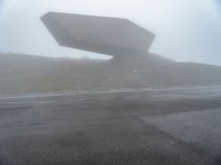 a car driving on the road during the foggy day in front of a large object