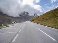 a wide empty road runs alongside the high mountains in a cloudy day with many clouds