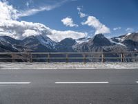 the mountains are covered with snow while the road passes by on a bridge across from them