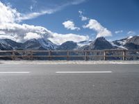 the mountains are covered with snow while the road passes by on a bridge across from them