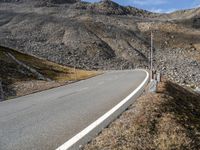 a road runs through a large rocky landscape with mountains in the distance, surrounded by barbed fence posts and rocks