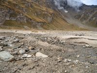 a dry, rocky ground surrounded by mountains and clouds covered with cloud covers, while clouds drift in between the top