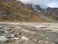 a dry, rocky ground surrounded by mountains and clouds covered with cloud covers, while clouds drift in between the top