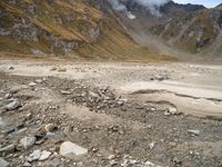 a dry, rocky ground surrounded by mountains and clouds covered with cloud covers, while clouds drift in between the top