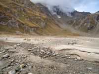 a dry, rocky ground surrounded by mountains and clouds covered with cloud covers, while clouds drift in between the top