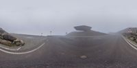 three roads surrounded by rocks and in the fog with a small building in the distance