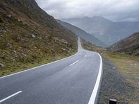 the empty winding road goes into the mountain valley on the left side with two large mountains in the distance