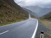 the empty winding road goes into the mountain valley on the left side with two large mountains in the distance