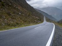 the empty winding road goes into the mountain valley on the left side with two large mountains in the distance