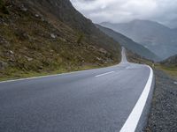 the empty winding road goes into the mountain valley on the left side with two large mountains in the distance