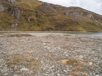 a small body of water surrounded by a mountainous area with rocks on it and grass in the middle of the picture