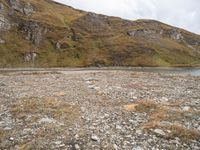 a small body of water surrounded by a mountainous area with rocks on it and grass in the middle of the picture