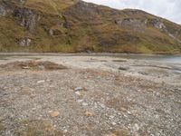 a small body of water surrounded by a mountainous area with rocks on it and grass in the middle of the picture