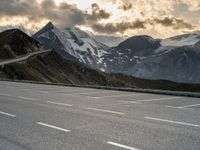 a mountain landscape showing a car parked on an empty parking lot next to snow covered mountains